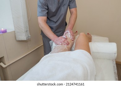 A male massage therapist massages female legs using a gentle body scrub. Foot scrub at the spa. Body care concept