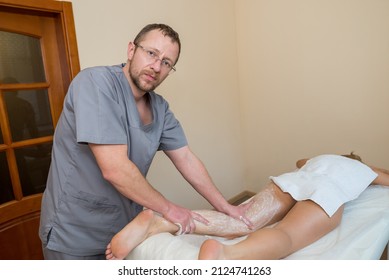 A male massage therapist massages female legs using a gentle body scrub. Foot scrub at the spa. Body care concept