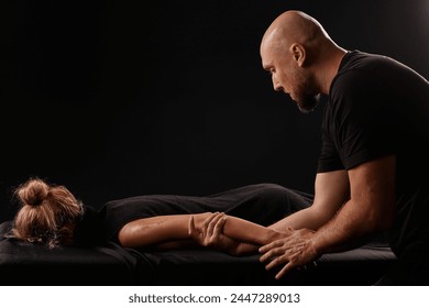 male masseur giving a hand massage to a girl on a dark background, hand massage - Powered by Shutterstock