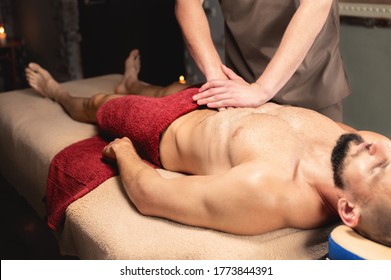 Male Masseur Massages The Thoracic Diaphragm Of A Muscular Male Athlete In A Massage Room With Dark Lighting