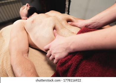 Male Masseur Massages The Thoracic Diaphragm Of A Muscular Male Athlete In A Massage Room With Dark Lighting