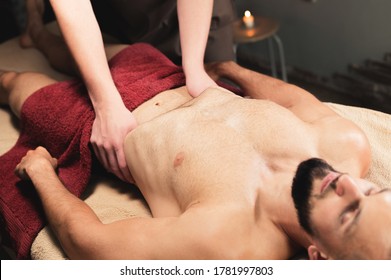 Male Masseur Massages The Thoracic Diaphragm Of A Muscular Male Athlete In A Massage Room With Dark Lighting