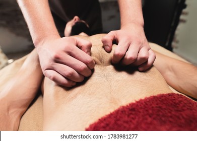 Male Masseur Massages The Thoracic Diaphragm Of A Muscular Male Athlete In A Massage Room With Dark Lighting