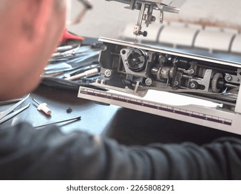 Male master repairs the sewing machine. Inspection of the mechanism in search of a breakdown. Professional adjustment of a sewing machine. Cleaning and repair of professional equipment. - Powered by Shutterstock