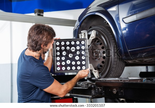 Male mechanic adjusting wheel alignment machine on\
car in garage