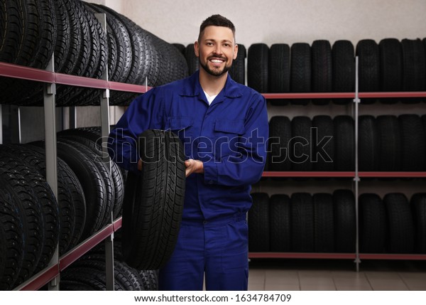 Male mechanic with\
car tire in auto store