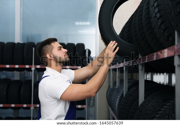 Male mechanic with\
car tire in auto store