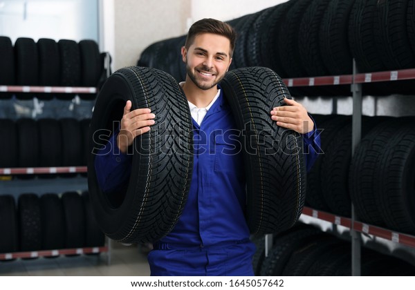 Male mechanic with\
car tires in auto store