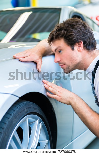 Male mechanic examine car finish on dents or scratches\
in workshop 