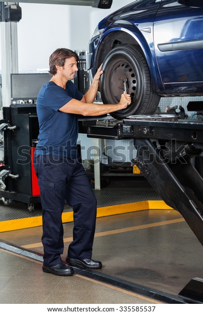 Male\
mechanic fixing lifted car tire at auto repair\
shop