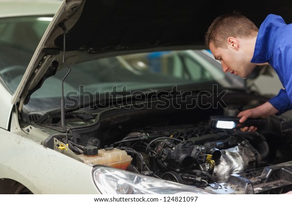 Male\
mechanic with flashlight examining car\
engine