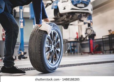 Male mechanic hold and rolling tire at repairing service garage background. Technician man replacing winter and summer tyre for safety road trip. Transportation and automotive maintenance concept