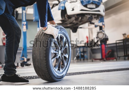 Male mechanic hold and rolling tire at repairing service garage background. Technician man replacing winter and summer tyre for safety road trip. Transportation and automotive maintenance concept