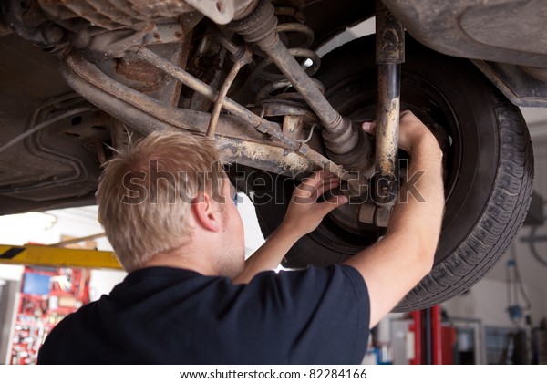 A male mechanic inspecting a CV joint on a car in an\
auto repair shop