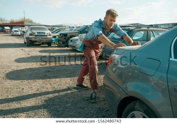 Male mechanic\
pushing the car on\
junkyard