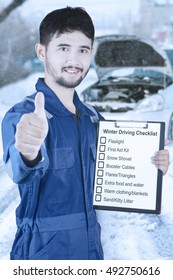 Male Mechanic Showing Thumb Up While Holding Clipboard With List Of Winter Driving Tips