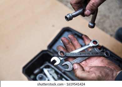 A male mechanic is sorting out wrenches in a box with tools for repair of faulty equipment. Hands smeared with grease are holding various wrenches. Workshop and repairing - Powered by Shutterstock