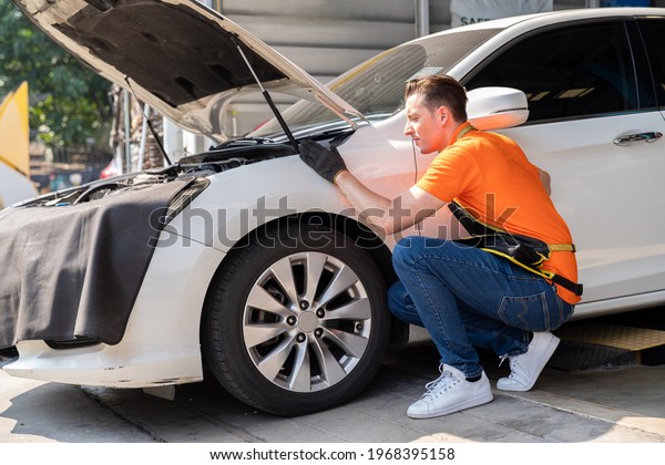 Male mechanic working at\
the garage. Male car mechanic examining, repair and maintenance\
under hood of car at auto car repair service. Car service and\
Maintenance concept