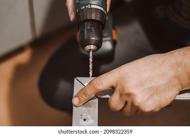 Male mechanic works in workshop with electric drill. Worker drills hole in metal. Lifestyle, professional activity. Hands hold a repair tool.