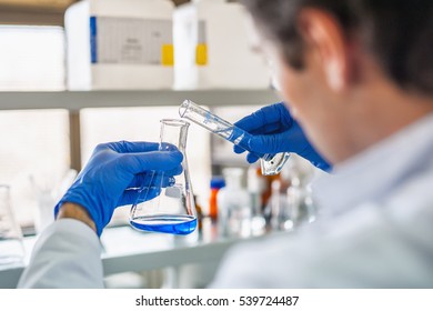 Male medical or scientific laboratory researcher performs tests with blue liquid. Close up