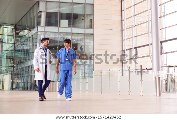 Male Medical Staff Talking As They Walk Through\
Lobby Of Modern Hospital\
Building