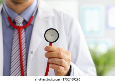 Male medicine doctor hand holding stethoscope head closeup in front of his chest. Healthy heart, eating and lifestyle, physician ready to examine patient, physical and disease prevention concept