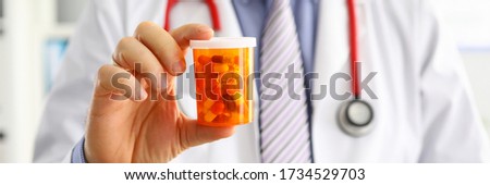 Male medicine doctor hand holding and offering to patient jar of pills. Medical care prescription pharmacology insurance concept. Giving or showing medications to patient. Physician ready to help