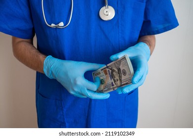 Male Medicine Doctor Holding In Hands Bunch Of Hundred Dollars Banknotes. Payment To Employees In The Red Zone. Award To Doctors Working With Covid Patients