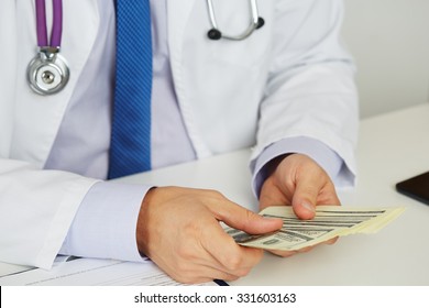 Male Medicine Doctor Holding In Hands Bunch Of Hundred Dollars Banknotes Counting Them. Medic Personnel Salary, Prestige And High Paid Job, Education, Public Health Business, Medical Insurance Concept