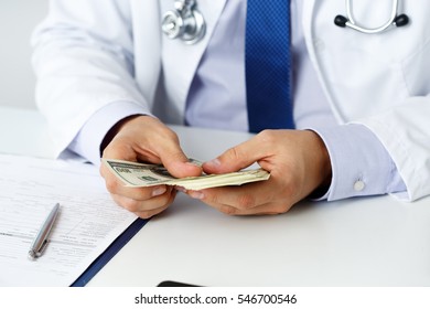 Male Medicine Doctor Holding In Hands Bunch Of Hundred Dollars Banknotes Counting Them. Medic Personnel Salary, Prestige And High Paid Job, Education, Public Health Business, Medical Insurance Concept