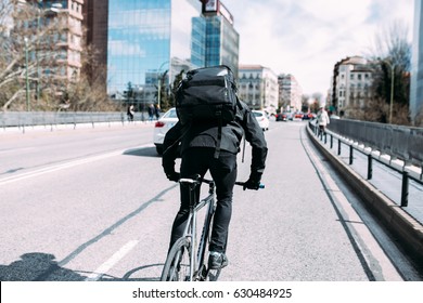 male Messanger riding fixed gear fixie bicycle around urban city of barcelona, spain with large black backpack bag making deliveries in soft light