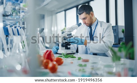 Male Microbiologist Puts Lab-Grown Cultured Vegan Meat Sample under Microscope for Analysis. Medical Scientist Working on Plant-Based Beef Substitute for Vegetarians in Modern Food Science Laboratory.