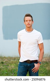 A Male Model Looks Directly At The Camera With His Hands In His Pockets While Wearing A White Tee Shirt.