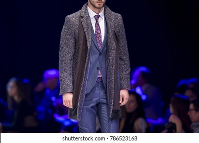 Male Model Walks The Runway In Stylish Suit During A Fashion Show. Fashion Catwalk Event Showing New Collection Of Clothes. Single Model. Blue Background.