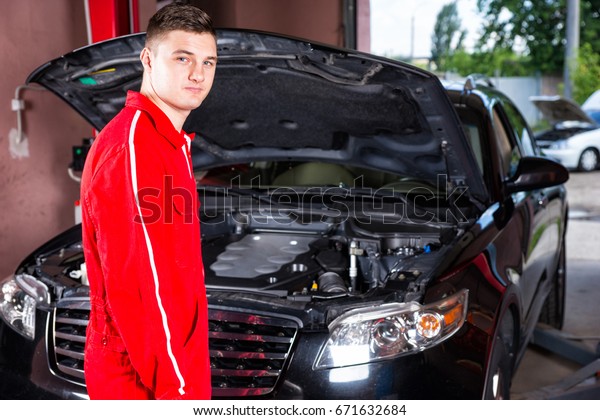 Male motor mechanic\
in uniform standing near a black sedan and going to diagnose the\
car in a garage workshop