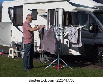 A male motorhome owner hangs his towel on a rotary clothes dryer with his recreational vehicle in the background. Sunny Day