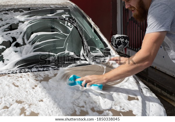 Male motorist\
washing car with a washcloth and shampoo, auto covered with foam,\
self-service car wash\
service