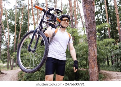 Male mountain biker carrying bicycle in the forest on a sunny day. - Powered by Shutterstock