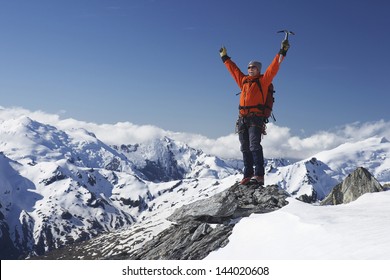 Male Mountain Climber Raising Hands With Icepick On Top Of Snowy Peak