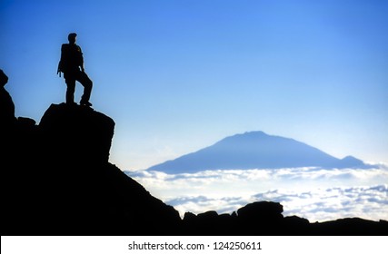 Male mountain climber standing on top of Mt Kilimanjaro with a view to Mt Meru. Mt. Kilimanjaro and Uhuru Peak at 5895m is the highest peak in Africa.