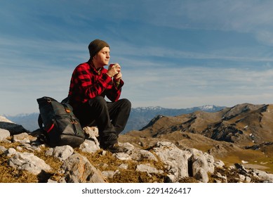 male mountaineer taking a break and drinking a beverage from a red cup while hiking in the mountains on a sunny day. sport and outdoor adventure - Powered by Shutterstock