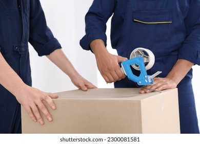 Male movers packing box with adhesive tape indoors, closeup - Shutterstock ID 2300081581