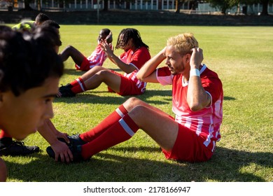 Male multiracial athletes holding legs of teammates doing crunches on grassy field at playground. Assisting, unaltered, soccer, sport, teamwork, competition, exercising, training and fitness. - Powered by Shutterstock