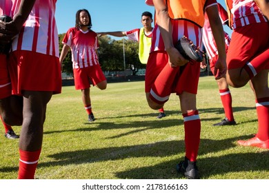 Male multiracial athletes in red uniforms stretching legs while exercising in playground in summer. Player, unaltered, soccer, sport, teamwork, competition, training and fitness concept. - Powered by Shutterstock