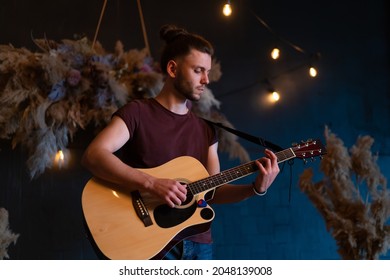 Male musician playing acoustic guitar. Guitarist plays classical guitar on stage in concert Handsome young hipster male guitar player perform private party Stylish long hair Medium shoot