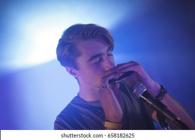 Male musician playing mouth organ in illuminated nightclub - Powered by Shutterstock