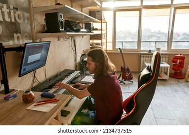 Male musician recording music on computer app while playing electronic piano at home studio. Concept of domestic hobby, entertainment and leisure. Young caucasian creative songwriter man sit at table