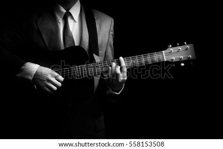 male musician in suit playing acoustic guitar, black and white. isolated on black