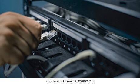 Male network administrator inserts cables into the server rack working with internet equipment in server room. Maintenance of LAN, computer networks and web servers. Data storage center. Close Up.