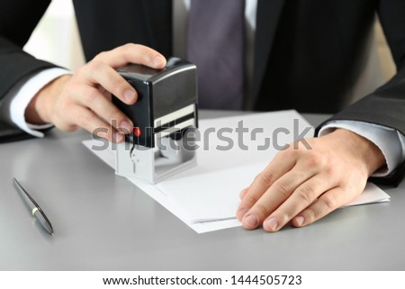 Male notary stamping document at table, closeup